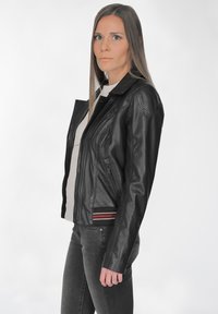 Schwarze Leder-Motorradjacke mit tailliertem Design, asymmetrischem Reißverschluss und roten Streifenakzenten am Saum. Normale Kragen und lange Ärmeln.