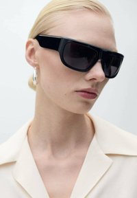 Black rectangular sunglasses with dark lenses, glossy frame, worn with a light-colored collared shirt, featuring silver hoop earrings.