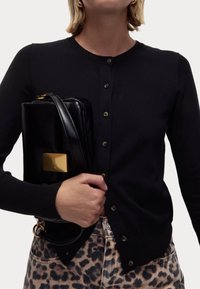 Czarny dzianinowy kardigan zapinany na guziki, w połączeniu z czarną błyszczącą torebką z złotym prostokątnym akcentem. Spodnie w cętki lamparta.