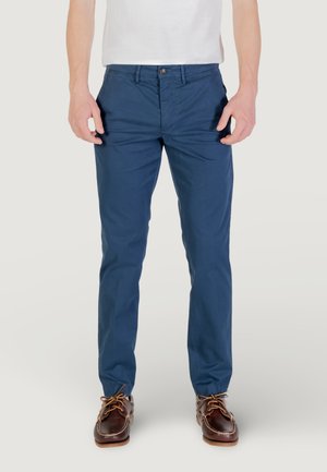 Chinos azul marino de corte slim, hechos de una tela ligera. Cuenta con un cierre de botón en la parte frontal y bolsillos laterales. Combinados con zapatos náuticos marrones.