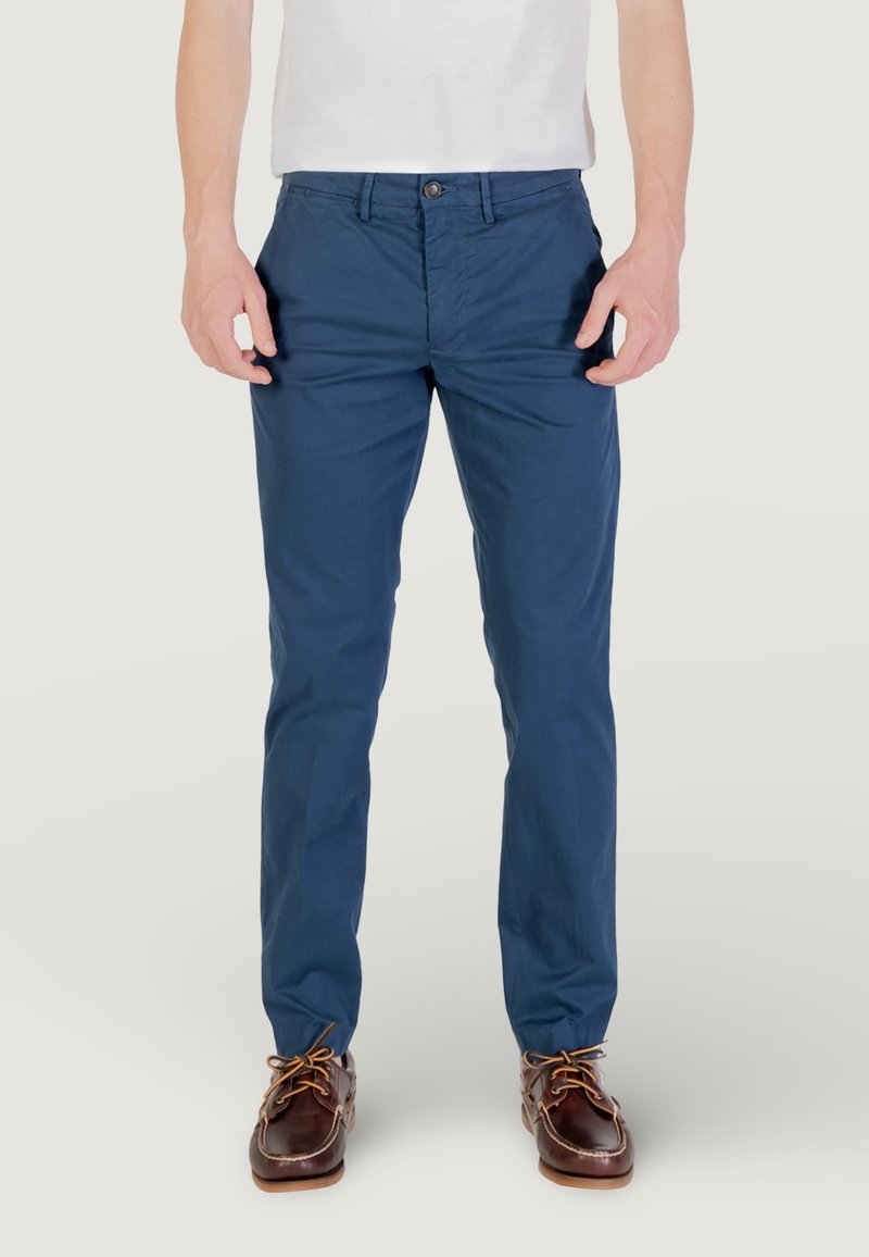 Chinos blu navy con una vestibilità slim, realizzati in tessuto leggero. Presentano una chiusura frontale con bottone e tasche laterali. Indossati con scarpe da barca marroni.