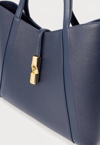 Tmavomodrá kožená kabelka s pevnou konštrukciou; má zlatý zámok a textúrovaný povrch s akcentmi na bočných paneloch.
