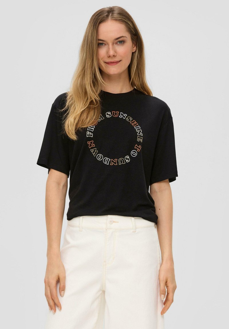 Zwarte katoenen T-shirt met een oversized pasvorm. Ronde witte en oranje tekstgrafiek gedrukt aan de voorkant. Korte mouwen en ronde hals.