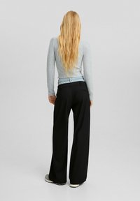 Ljusgrå långärmad tröja som kombineras med vida svarta byxor; synlig denimdetalj vid midjan; strukturerad tyg, rak silhuett.