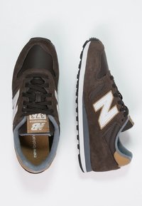 Baskets en suède et cuir marron avec des accents blancs, design à lacets, col rembourré et semelle extérieure en caoutchouc noir. Présentant un patin de talon beige.