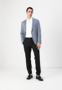 Light blue blazer over a white shirt, paired with black trousers. Notable details include structured lapels and a smooth fabric texture. Black shoes complete the look.