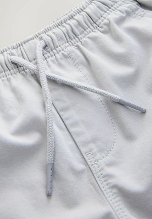 Svetlosivé šortky s elastickým pásom, ktoré majú šnúrku na stiahnutie, ploché švy a hladkú textúru látky.