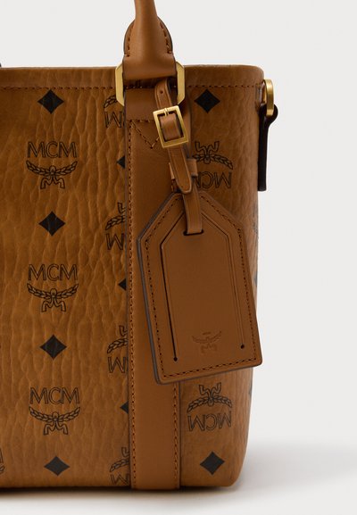 Sac à main en cuir marron avec logo MCM embossé, motif en losanges et ferrures dorées. Comprend une étiquette en cuir attachée par une sangle.
