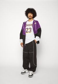 Lilla og sort jakke med hætte, hvid Lakers trøje med nummer 23, sorte bukser med hvide detaljer, sorte og hvide sneakers.
