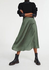 Grøn blomster midi-skjørt med en flydende silhuet, lavet af glat materiale, parret med sorte ankelstøvler og en sort sweater.