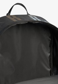 Rucsac negru cu un exterior neted, formă rotundă și un mâner de sus. În interior, are un căptușeală moale și texturată cu un închizător cu fermoar.