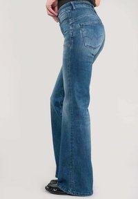 Jeans en denim bleu évasés avec une taille moyenne. Comprend cinq poches et un léger dégradé. Fabriqué en tissu doux et extensible.