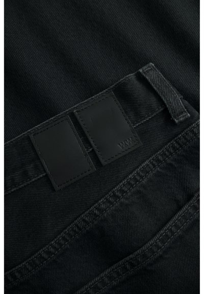 Zwarte denim jeans met een gestructureerd oppervlak, voorzien van twee rechthoekige leren patches dicht bij de tailleband en contrasterende stikdetails.