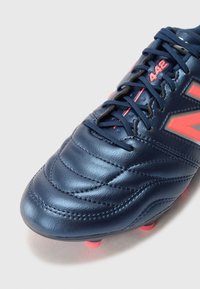Crampon de football en cuir bleu marine avec des coutures texturées, des accents rouges et des lacets noirs. Présente quatre crampons roses sur la semelle pour une meilleure traction.