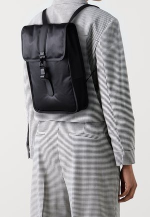 Sort nylonrygsæk med klaplukning og justerbare stropper, der har en glat tekstur og minimalistisk design.