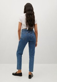 Jeans de mezclilla azul de cintura alta con pierna recta, cinco bolsillos y costuras cosidas, acompañados de zapatos negros.