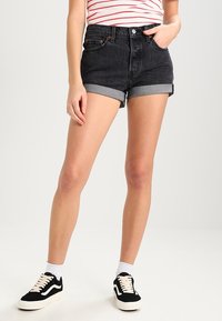 Shorts de mezclilla negra con dobladillos enrollados, cintura alta y bolsillos frontales. Combinados con una blusa a rayas y zapatillas de ante negras con cordones blancos.
