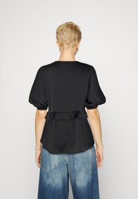 Top nero con maniche a sbuffo e dettaglio arricciato in vita, realizzato in tessuto morbido e liscio, con un design dritto sul retro. Indossato con pantaloni di denim a gamba larga.