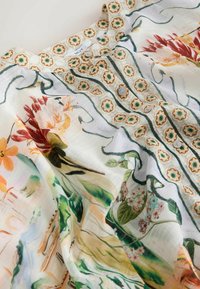 Bluza din material alb transparent, imprimată cu flori, prezentând modele detaliate de viță verde, flori portocalii, roșii și galbene, cu nasturi mici.