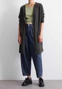 Long dark gray cardigan with hood, two front pockets, worn over a light green crop top and loose blue denim jeans, paired with black shoes.
