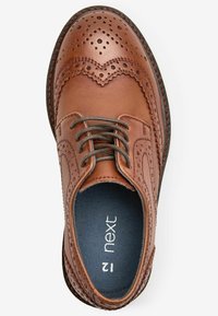 Chaussure à lacets en cuir marron avec des perforations décoratives, design de brogue, bout rond et lacets gris foncé. Logo de la marque visible à l'intérieur.