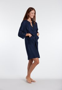 Abito blu navy, lungo fino al ginocchio, realizzato in tessuto morbido, con scollatura a V, maniche lunghe e due tasche frontali, progettato per il comfort.