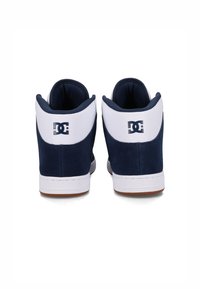 Vysoké tenisky s horným strihom, ktoré majú námornícky zamak a bielu koženú hornú časť, bielu gumovú podrážku a viditeľné logo na zadnej strane.