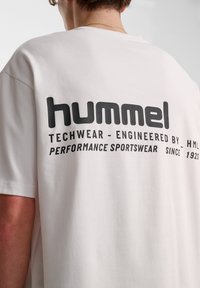 Vit techwear t-shirt med avslappnad passform. Har svart tryckt logotyp på ryggen som framhäver "hummel" och andra textdetaljer.