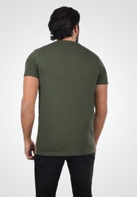 Olivengrøn kortærmet T-shirt lavet af bomuld. Tætsiddende design med rund hals og glat tekstur. Båret med mørke jeans.