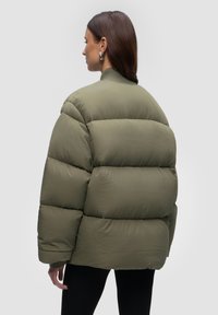 Olive green puffer jacket with a boxy design, ribbed collar, and quilted texture. Features large puffed sections for insulation.