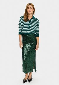 Striped green and white polo shirt with a collar; paired with a fitted, sequined green skirt featuring a side slit; black pointed shoes.