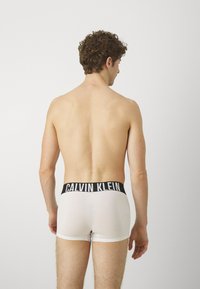 Hvite boksershorts med en svart Calvin Klein-logo på linningen, glatt tekstur, tettsittende design og lengde til midt på låret.