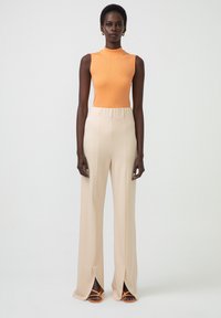 Top ușor, cu dungi verticale, de culoare portocalie, fără mâneci, purtat cu pantaloni beige cu talie înaltă și croială largă, prevăzuți cu fante laterale, și sandale portocalii cu barete.