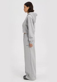 Lichtgrijze cropped hoodie met een capuchon, gecombineerd met losvallende grijze joggingsbroek. Heeft ribgebreide manchetten en minimalistische branding.