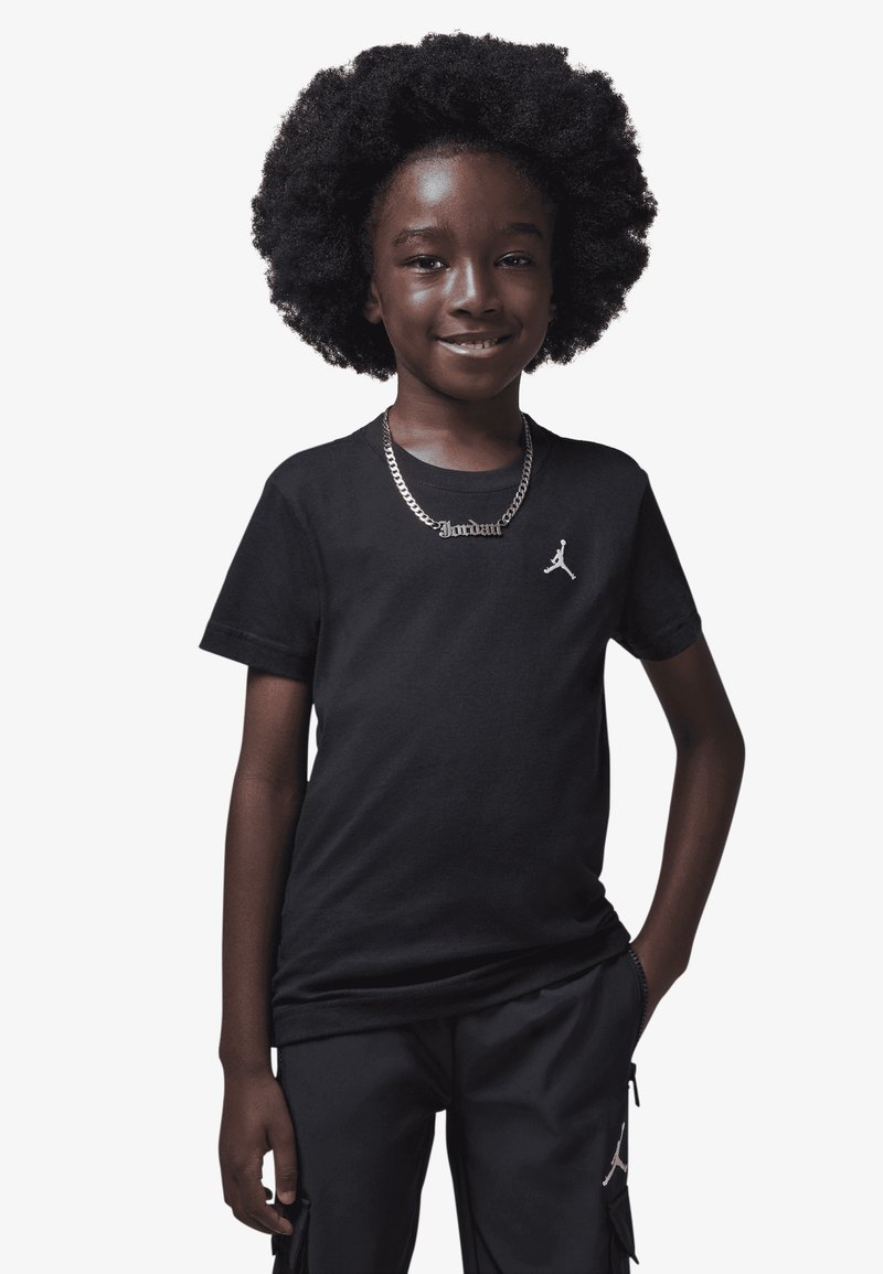 Svart bomulls-T-skjorte med rund hals og en liten hvit Jordan-logo på brystet, kombinert med svarte cargoshorts. Sølvkjede.