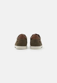 Baskets en cuir marron et en tissu avec une surface texturée et des semelles en caoutchouc blanches, avec des accents marron sur le talon et les lacets.