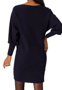 Abito maglione lavorato a maglia di colore navy con taglio morbido, maniche raglan, texture a coste e lunghezza a metà coscia. Dettagli delle cuciture sottili in tutta la sua superficie.