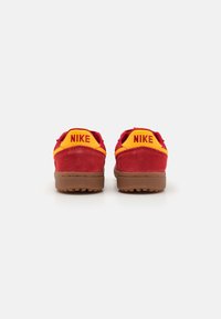 Rote und gelbe Nike-Sneaker mit einem Obermaterial aus Wildleder, einer Gummisohle und "NIKE"-Branding auf der Ferse in fetten Buchstaben.
