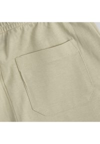 Tissu en coton beige clair comportant une seule poche à rabat de forme carrée avec des détails de couture subtils. La texture semble lisse.