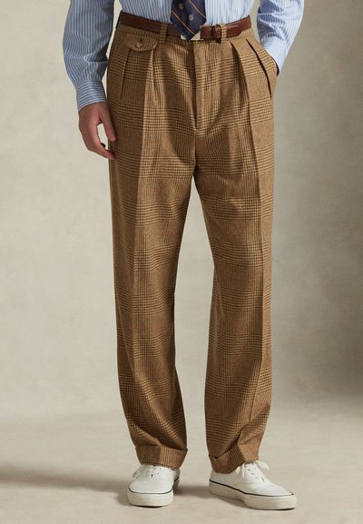 �Καφέ καρό παντελόνι με φαρδιά γραμμή, πλισέ μπροστά και έντονες πτυχές. Συνδυάζεται με μπλε ριγέ πουκάμισο και λευκά αθλητικά παπούτσια.