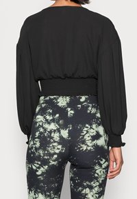 Blusa nera corta con maniche lunghe e vita arricciata, abbinata a leggings a vita alta con un motivo tie-dye verde e nero.
