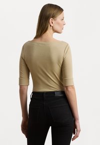 Beige tettskjorte med bred utringing og trekvartlange ermer, sammen med svarte høytlivte jeans med baklommer og en teksturert midjebånd.