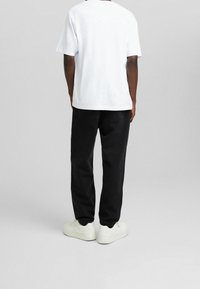 Camiseta de algodón blanca de manga corta, combinada con pantalones de mezclilla negros y zapatillas blancas, mostrando un ajuste relajado desde la vista trasera.