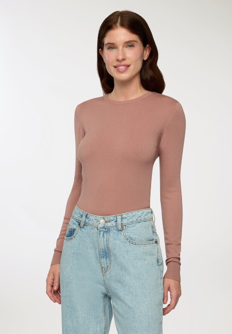 Długo rękawowy sweter w jasnoróżowym kolorze, z okrągłym dekoltem i dopasowanym krojem, w połączeniu z jasnoniebieskimi dżinsami z wysokim stanem.