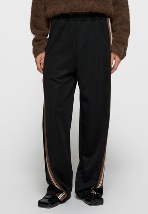 Czarne sportowe spodnie z brązowo-białymi bocznymi paskami, elastycznym pasem i subtelnym logo. Lekki materiał, luźny fason.