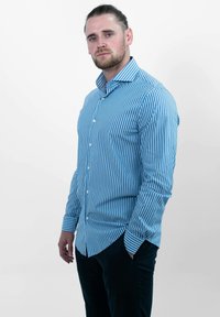 Blauwe gestreepte overhemd met lange mouwen, voorzien van verticale witte strepen, een puntige kraag en een gebogen zoom, gecombineerd met donkere broek.