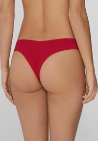 Braga de bikini roja con textura acanalada, diseño de tiro bajo y cobertura mínima en la parte trasera. Costuras lisas en los bordes.