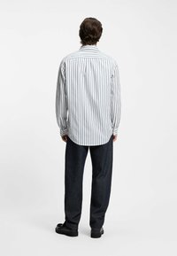 Weißes Hemd mit navyfarbenen vertikalen Streifen, langen Ärmeln, entspannter Passform und spitzem Kragen, kombiniert mit dunklen Jeans und schwarzen Schuhen.