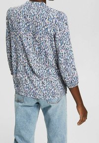 Blouse multicolore avec un motif texturé en bleu, rose et blanc. Dotée de manches trois-quarts, d'un détail froncé aux épaules et d'un col rond.