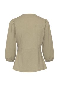 Blouse beige à manches longues avec manches bouffantes, légers fronces aux épaules et taille cintrée s'évasant doucement aux hanches.